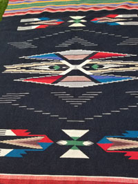 New Mexican vintage textiles, and Chimayo vintage blankets and textiles, a stunning vintage Chimayo textile with a black field, bands of colors, and brocade-work in the two end bands, Chimayo, New Mexico, c. 1930's. Closeup photo of the textile showing the beautiful center medallion.